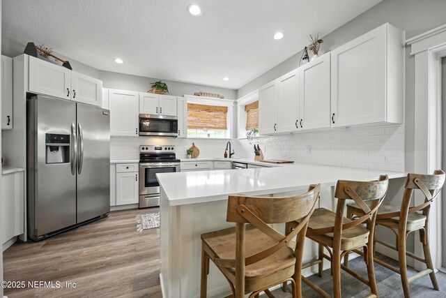 309 Elza Ln, Saint Augustine, FL 32086 - kitchen with stainless steel appliances, a breakfast bar area, wood finished floors, a peninsula, and white cabinetry