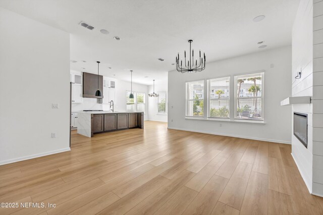 329 Rum Runner Way, Saint Johns, FL 32259 - unfurnished living room with a chandelier, a sink, a large fireplace, light wood-style flooring, and baseboards