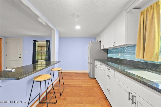 381 Bird Rd, Jacksonville, FL 32218 - kitchen featuring a kitchen bar, a textured ceiling, light wood-style flooring, white cabinets, and baseboards