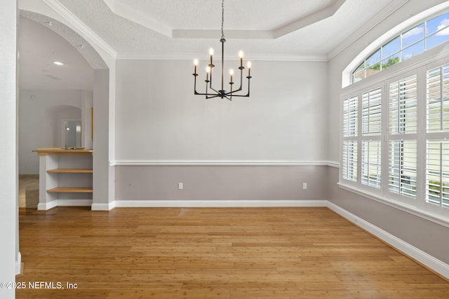 2305 Range Crescent Ct, Fleming Island, FL 32003 - empty room featuring a tray ceiling, a chandelier, light wood-style flooring, arched walkways, and ornamental molding