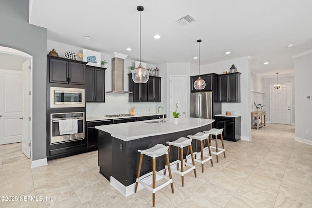 80 Atlas Dr, Saint Augustine, FL 32092 - kitchen featuring appliances with stainless steel finishes, wall chimney exhaust hood, backsplash, dark cabinets, and a kitchen island with sink