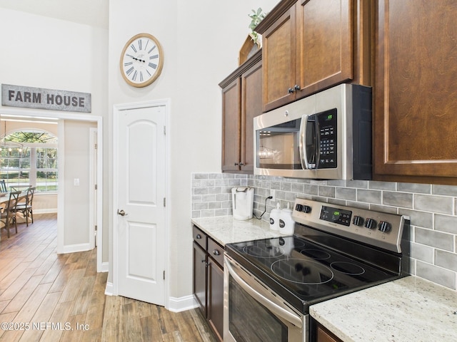 88137 Maybourne Rd, Yulee, FL 32097 - kitchen featuring stainless steel appliances, light stone countertops, baseboards, light wood-type flooring, and decorative backsplash