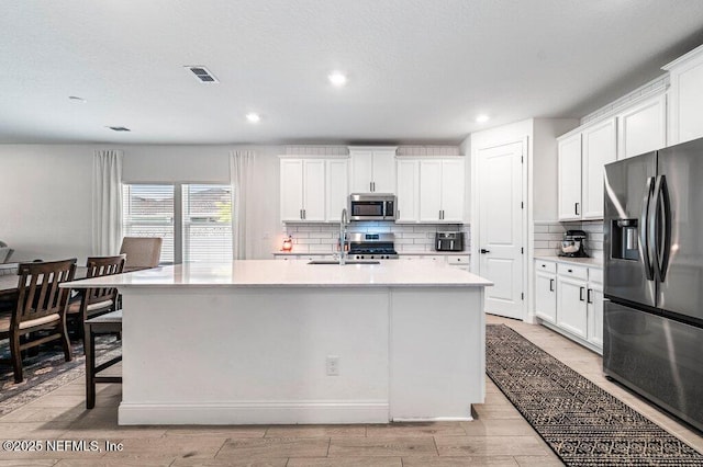 154 Pine Candle Way, Saint Augustine, FL 32092 - kitchen with appliances with stainless steel finishes, a sink, an island with sink, decorative backsplash, and light wood finished floors