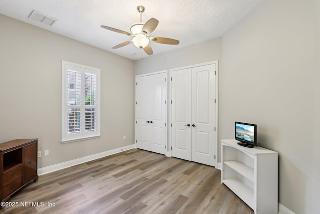 182 Malley Cove Ln, Fleming Island, FL 32003 - unfurnished bedroom featuring multiple closets, light wood-style flooring, baseboards, a textured ceiling, and ceiling fan