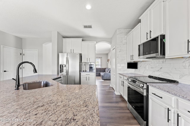 1578 Harvest Cove Dr, Middleburg, FL 32068 - kitchen featuring a sink, stainless steel appliances, arched walkways, light stone counters, and white cabinetry
