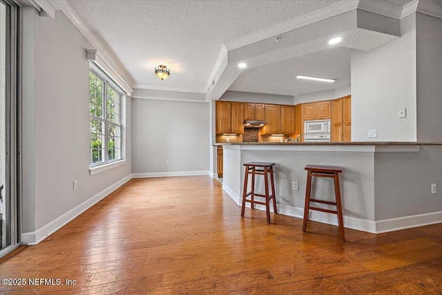 215 S Ocean Grande Dr Unit 105, Ponte Vedra Beach, FL 32082 - kitchen featuring white microwave, a textured ceiling, ornamental molding, light wood-style floors, and under cabinet range hood