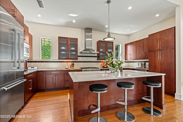 295 Sophia Ter, Saint Augustine, FL 32095 - kitchen with wall chimney range hood, stainless steel appliances, light wood-style flooring, a breakfast bar area, and light countertops