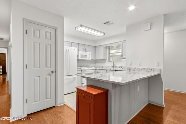 13674 Wm Davis Pkwy, Jacksonville, FL 32224 - kitchen featuring white appliances, a peninsula, a kitchen breakfast bar, light wood-style flooring, and light stone countertops