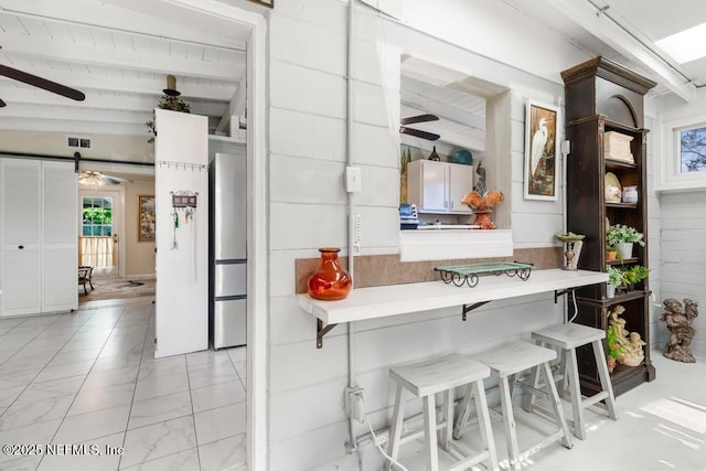 1810 Griflet Rd, Jacksonville, FL 32211 - kitchen featuring ceiling fan, freestanding refrigerator, light marble finish floors, a kitchen bar, and beamed ceiling