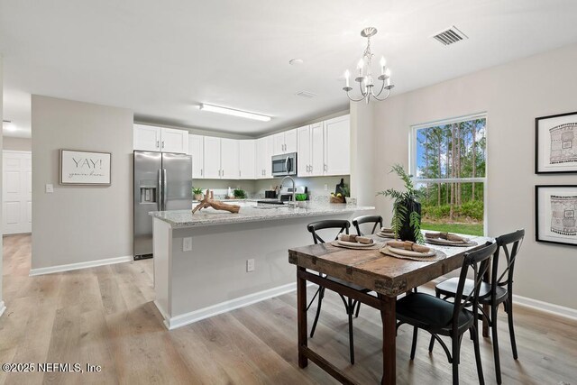 889 Aiken St, Saint Augustine, FL 32084 - kitchen with appliances with stainless steel finishes, a peninsula, white cabinetry, a chandelier, and light wood finished floors