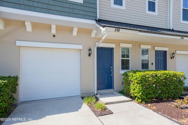 246 Moultrie Village Ln, Saint Augustine, FL 32086 - view of exterior entry featuring a garage, driveway, a shingled roof, and stucco siding