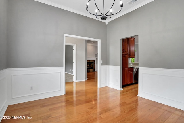 880 Buckeye Ln W, Saint Johns, FL 32259 - empty room featuring a chandelier, crown molding, light wood-type flooring, a tiled fireplace, and wainscoting