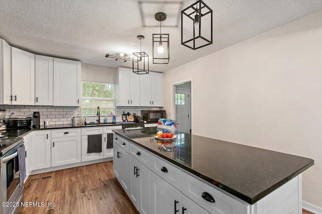 3020 Gilmore St, Jacksonville, FL 32205 - kitchen featuring black microwave, decorative backsplash, wood finished floors, stainless steel range with electric stovetop, and white cabinetry