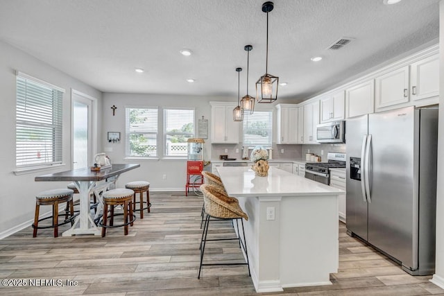4604 Clapboard Crossing Way, Jacksonville, FL 32226 - kitchen with appliances with stainless steel finishes, white cabinets, light wood finished floors, a kitchen island, and recessed lighting