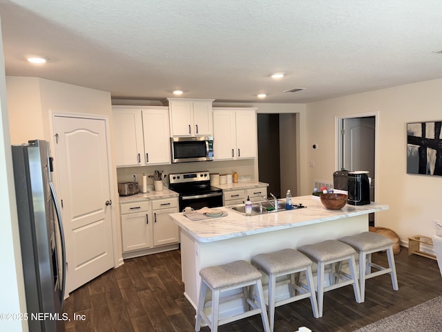 126 Falcon Ridge Rd, Saint Augustine, FL 32084 - kitchen featuring stainless steel appliances, dark wood-style flooring, white cabinets, a kitchen bar, and an island with sink
