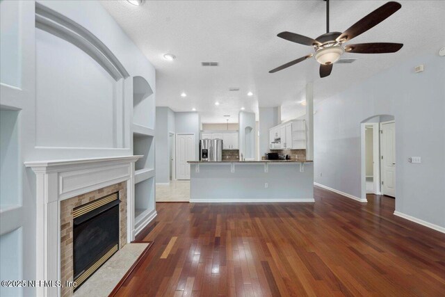 8681 Canopy Oaks Dr, Jacksonville, FL 32256 - unfurnished living room featuring dark wood-type flooring, ceiling fan, a fireplace with flush hearth, baseboards, and arched walkways