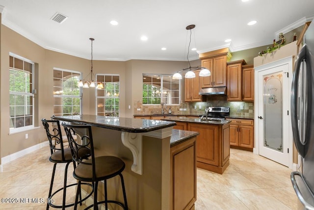 69 Bridle Ridge Ct, Flagler Beach, FL 32136 - kitchen featuring a center island, under cabinet range hood, appliances with stainless steel finishes, brown cabinets, and backsplash