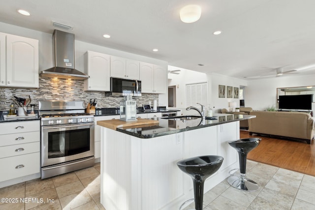 1912 Sunrise Dr, Fernandina Beach, FL 32034 - kitchen with stainless steel range with gas stovetop, wall chimney exhaust hood, ceiling fan, a breakfast bar area, and white cabinetry