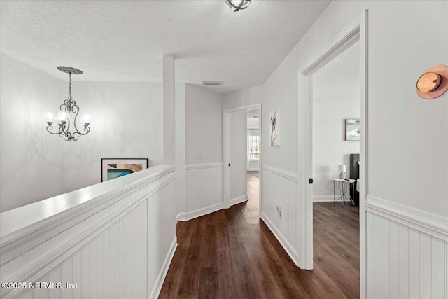 28 S Comares Ave, Saint Augustine Beach, FL 32080 - corridor featuring dark wood-type flooring, a textured ceiling, a chandelier, and wainscoting