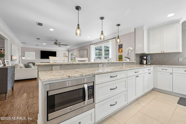 2808 Scott Mill Estates Dr, Jacksonville, FL 32257 - kitchen with crown molding, stainless steel microwave, a peninsula, white cabinets, and hanging light fixtures