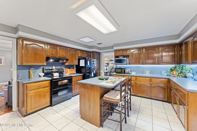 2364 Smullian Trl S, Jacksonville, FL 32217 - kitchen with black appliances, under cabinet range hood, a kitchen island, light countertops, and a breakfast bar