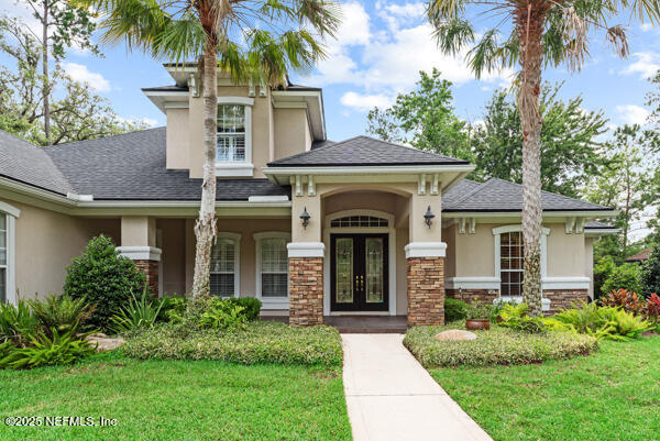 1821 Wind Ridge Ct, Fleming Island, FL 32003 - view of front of house featuring french doors, stucco siding, a front yard, roof with shingles, and stone siding