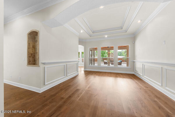 1821 Wind Ridge Ct, Fleming Island, FL 32003 - unfurnished living room featuring arched walkways, wood finished floors, a decorative wall, a wainscoted wall, and ornamental molding