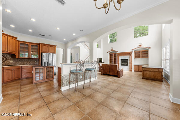 1821 Wind Ridge Ct, Fleming Island, FL 32003 - kitchen featuring brown cabinetry, light tile patterned floors, stainless steel fridge with ice dispenser, a chandelier, and arched walkways
