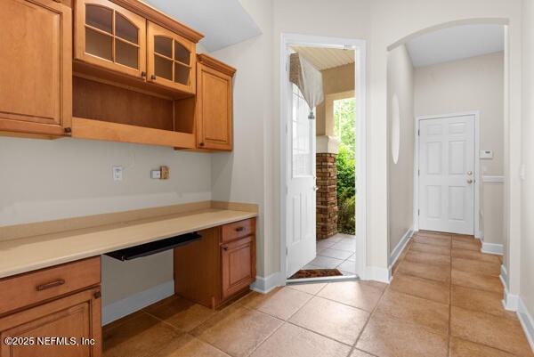 1821 Wind Ridge Ct, Fleming Island, FL 32003 - kitchen with arched walkways, light tile patterned floors, light countertops, glass insert cabinets, and brown cabinetry