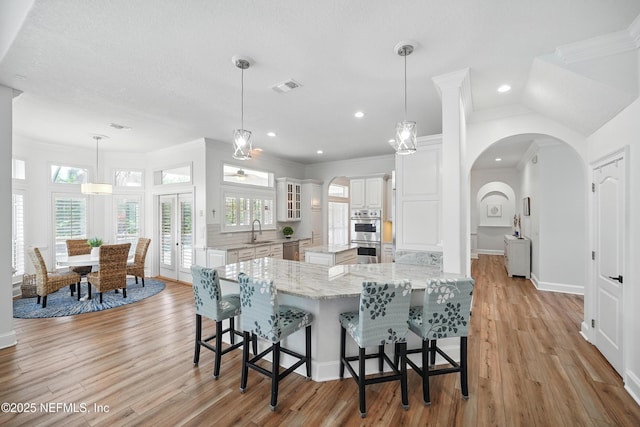 4427 Royal Tern Ct, Jacksonville Beach, FL 32250 - kitchen with stainless steel appliances, a center island, light wood-type flooring, white cabinetry, and crown molding