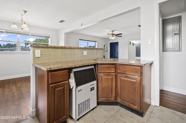 3121 Holly Berry Ln, Jacksonville, FL 32277 - kitchen with a ceiling fan, brown cabinets, light stone countertops, a textured ceiling, and pendant lighting