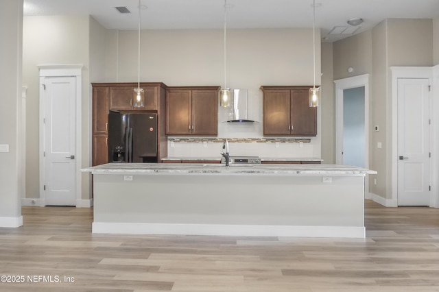 11 Woodstone Ln, Palm Coast, FL 32164 - kitchen featuring black refrigerator with ice dispenser, wall chimney exhaust hood, light wood-style flooring, a kitchen island with sink, and backsplash