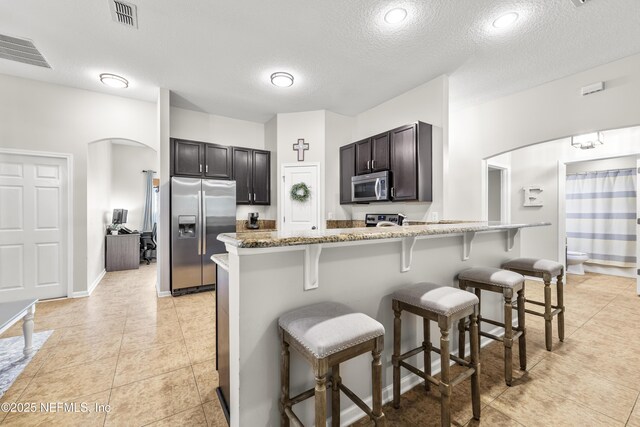 81014 Lockhaven Dr, Yulee, FL 32097 - kitchen with appliances with stainless steel finishes, a textured ceiling, a breakfast bar area, arched walkways, and light stone countertops