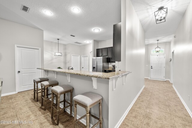 81014 Lockhaven Dr, Yulee, FL 32097 - kitchen with stainless steel refrigerator with ice dispenser, a textured ceiling, a kitchen breakfast bar, light tile patterned floors, and light stone counters