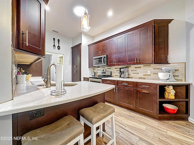 3923 Eden Estate Trl, Middleburg, FL 32068 - kitchen with appliances with stainless steel finishes, a peninsula, decorative backsplash, a kitchen breakfast bar, and light wood finished floors