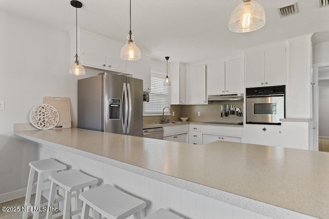 416 Margaret St, Neptune Beach, FL 32266 - kitchen with appliances with stainless steel finishes, a sink, white cabinetry, under cabinet range hood, and a peninsula