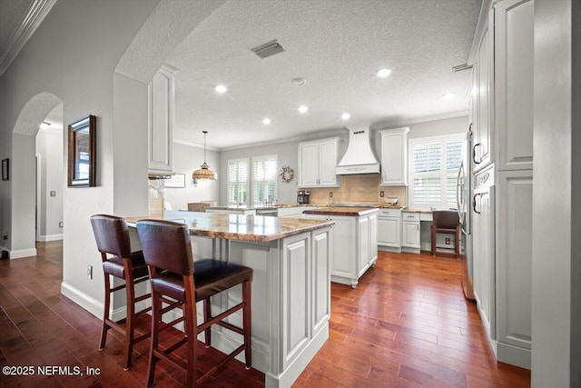 1714 Chatham Village Dr, Fleming Island, FL 32003 - kitchen featuring custom exhaust hood, crown molding, arched walkways, a peninsula, and a breakfast bar