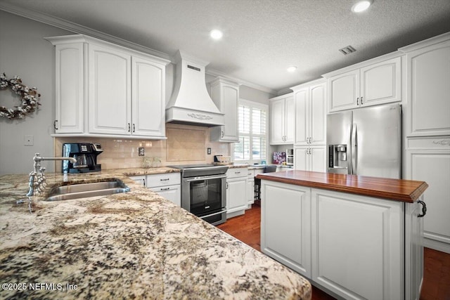 1714 Chatham Village Dr, Fleming Island, FL 32003 - kitchen featuring appliances with stainless steel finishes, custom exhaust hood, white cabinetry, crown molding, and recessed lighting