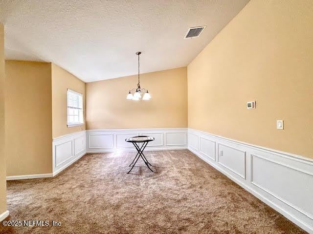 8561 Little Swift Cir Unit 32D, Jacksonville, FL 32256 - carpeted empty room featuring a chandelier, lofted ceiling, a decorative wall, a wainscoted wall, and a textured ceiling