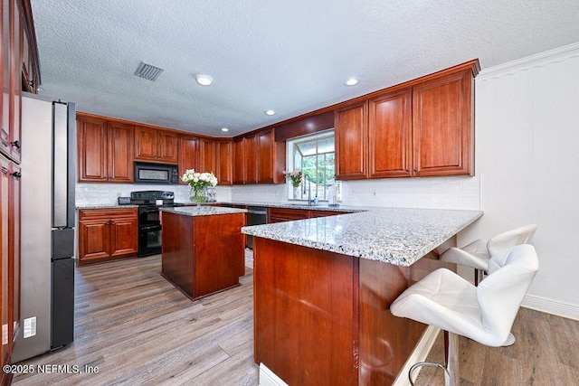 4966 Harvey Grant Rd, Fleming Island, FL 32003 - kitchen with black appliances, light wood-style flooring, a peninsula, a textured ceiling, and light stone counters