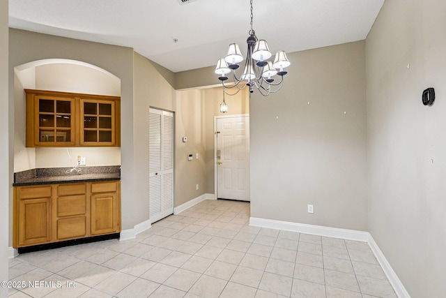 8601 Beach Blvd Unit 507, Jacksonville, FL 32216 - kitchen with a chandelier, glass insert cabinets, light tile patterned floors, baseboards, and brown cabinets