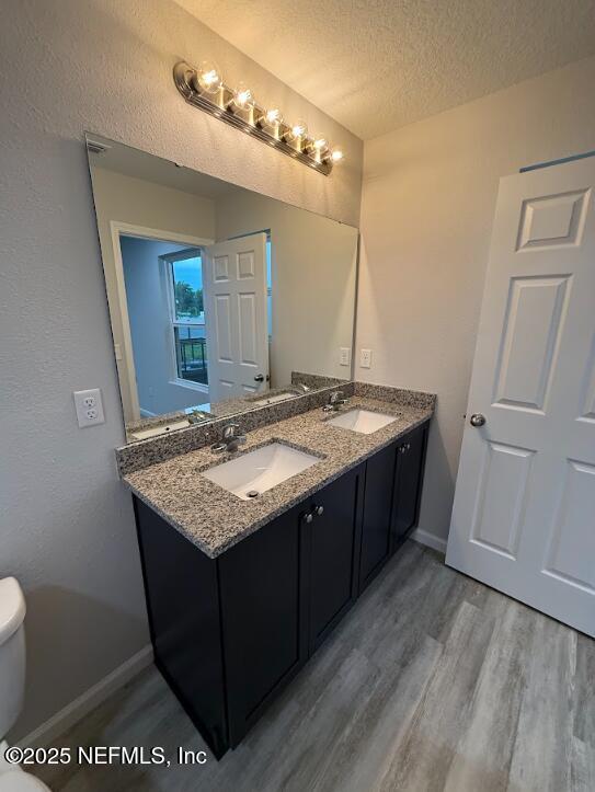 8051 Driggers St, Jacksonville, FL 32220 - bathroom featuring wood finished floors, double vanity, toilet, a textured ceiling, and baseboards