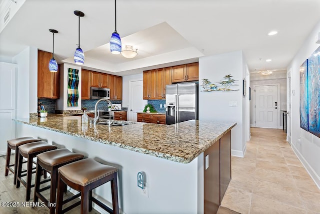 525 3rd St S Unit 513, Jacksonville Beach, FL 32250 - kitchen featuring appliances with stainless steel finishes, brown cabinets, light stone counters, a peninsula, and tasteful backsplash