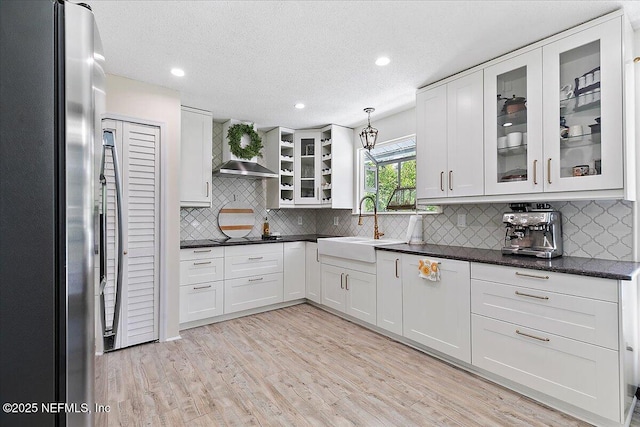 5265 State Rd 13 N, Saint Augustine, FL 32092 - kitchen with freestanding refrigerator, wall chimney range hood, light wood-style flooring, white cabinetry, and decorative backsplash
