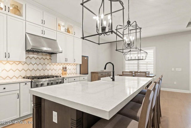 87 Tradesman Ln, Saint Johns, FL 32259 - kitchen featuring under cabinet range hood, a chandelier, a kitchen island with sink, tasteful backsplash, and white cabinets
