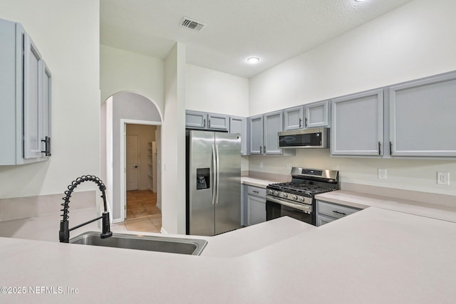 1867 Willesdon Dr E, Jacksonville, FL 32246 - kitchen with stainless steel appliances, arched walkways, light countertops, gray cabinets, and light tile patterned floors