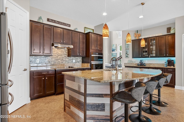 2148 S Sorrento Hills Rd, Saint Augustine, FL 32092 - kitchen featuring stainless steel appliances, a breakfast bar area, a kitchen island with sink, light stone counters, and under cabinet range hood