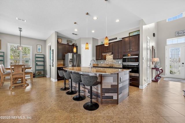 2148 S Sorrento Hills Rd, Saint Augustine, FL 32092 - kitchen with stainless steel fridge, dark brown cabinets, decorative backsplash, light stone countertops, and recessed lighting
