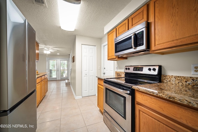 10571 Fox Squirrel Ct, Jacksonville, FL 32257 - kitchen featuring appliances with stainless steel finishes, light tile patterned flooring, brown cabinets, a textured ceiling, and a ceiling fan