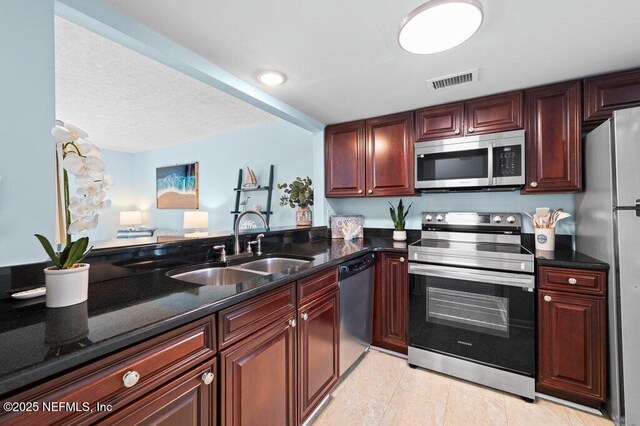 3145 Coastal Hwy Unit 1162, Saint Augustine, FL 32084 - kitchen featuring appliances with stainless steel finishes, a sink, reddish brown cabinets, dark stone countertops, and light tile patterned floors